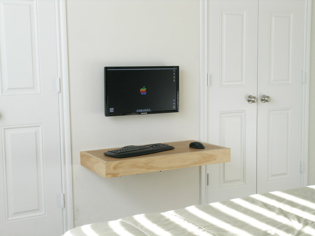 Minimalistischer Arbeitsplatz mit an der Wand montiertem Bildschirm, schwebendem Holzregal, Tastatur und Maus