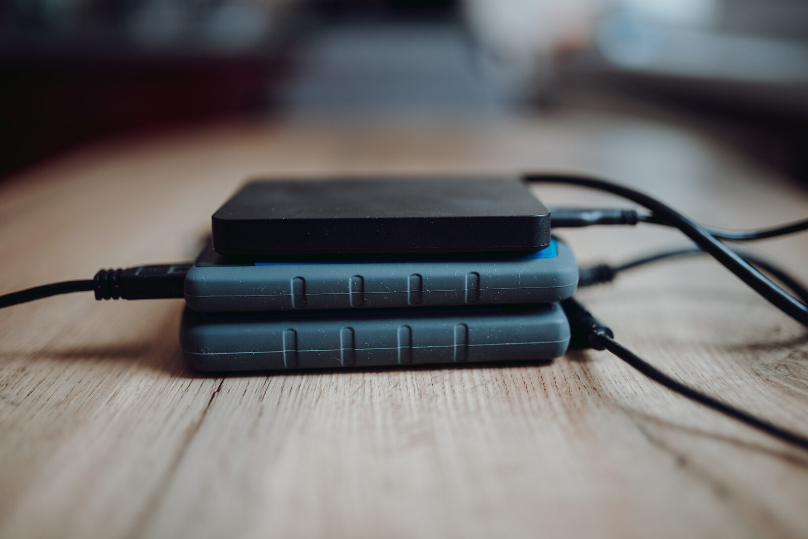 Drei externe Festplatten mit angeschlossenen USB-Kabeln, aufeinandergestapelt auf einem Holztisch