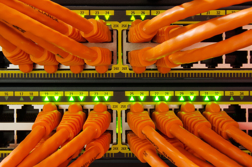 Netzwerk-Switch mit vielen orangefarbenen Patchkabeln und grün leuchtenden Port-Anzeigen