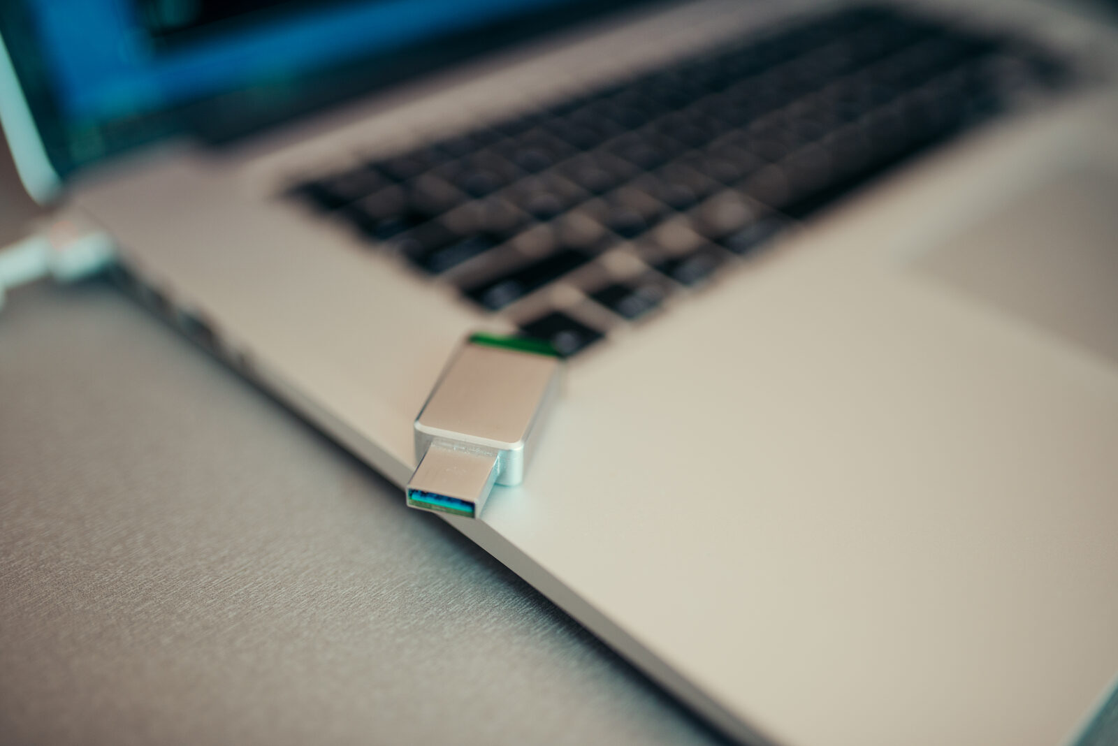 Kleiner USB-Stick aus Metall steckt seitlich in einem silbernen Laptop